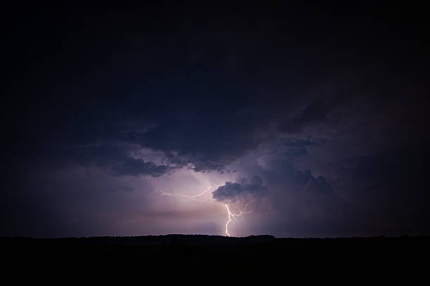 A dramatic photograph of a lightning strike illuminating the storm clouds in the dark night sky. The bolt branches through the atmosphere, creating a powerful display of nature's energy