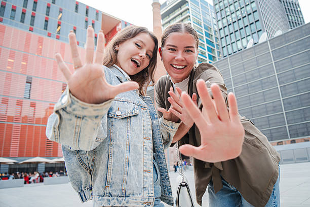 istock Two smiling young women playfully reaching out their hands toward the camera, creating a sense of interaction and joy, with a focus on their expressions and dynamic gesture. 2211288175