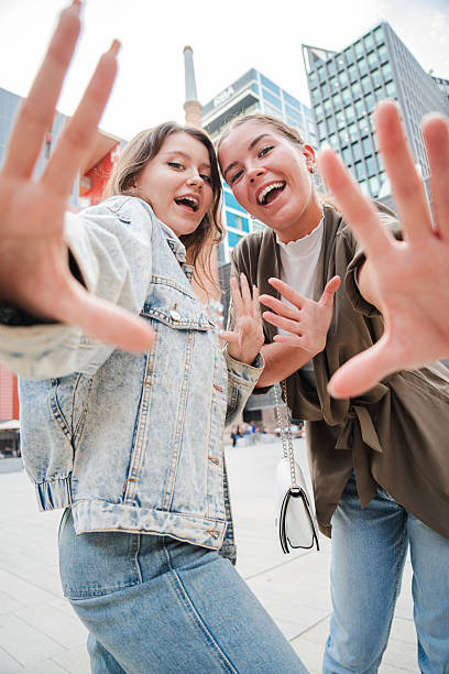 istock Vertical. Two smiling young women playfully reaching out their hands toward the camera, creating a sense of interaction and joy, with a focus on their expressions and dynamic gesture. 2211288874