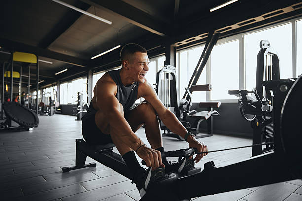 Cheerful attractive man smiling while using rowing machine in contemporary gym