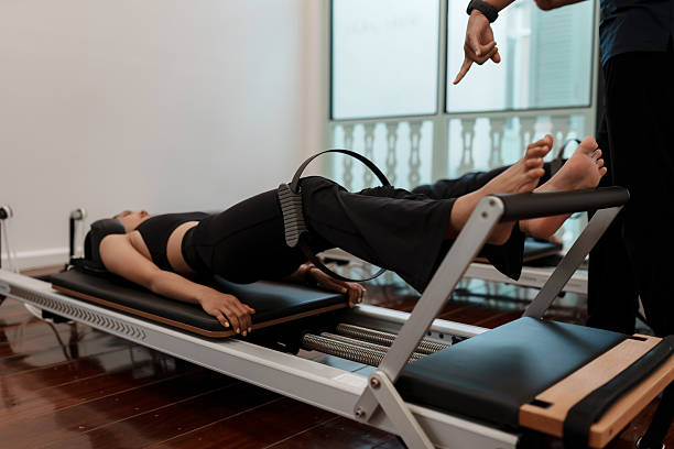 istock A woman using a Pilates ring between her knees while lying on a reformer. leg and core engagement during Pilates workout in studio fitness. Selective focus ring. 2211303069