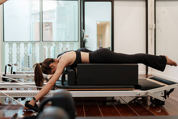 istock Asian woman practicing Pilates in a prone extension pose while pulling resistance straps on a reformer. 2211303093