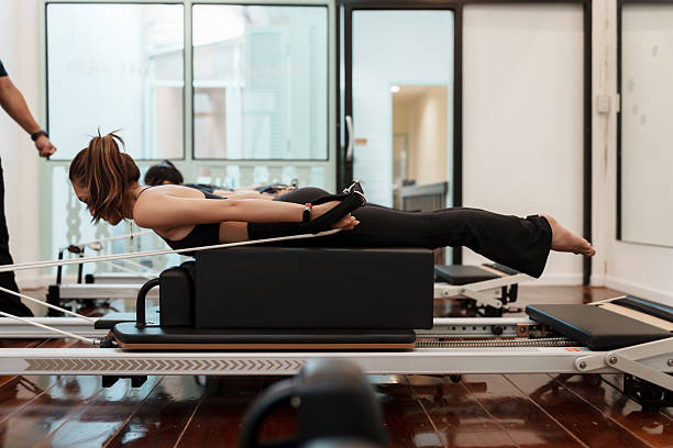istock Asian woman practicing Pilates in a prone extension pose while pulling resistance straps on a reformer. The image captures core strength, back activation, and full-body alignment in wellness studio. 2211303094