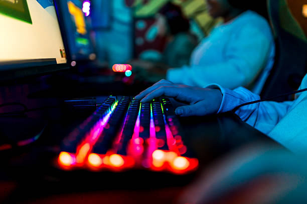Close-up of a gamer's hand playing on a colorful backlit keyboard in a dark room, creating an immersive gaming experience