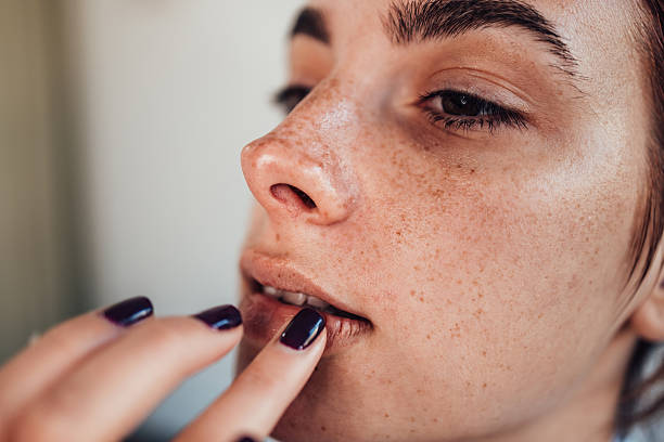 Make-up artist applying dark lipstick on freckled model's lips