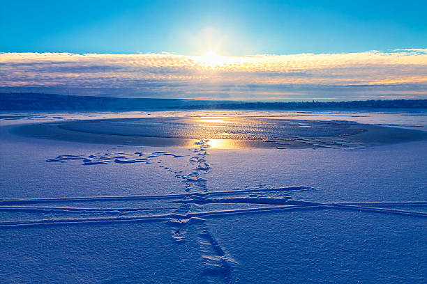 Snowy path leads to serene frozen lake under sunset