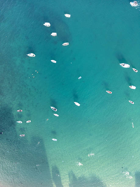 Aerial scene showing small boats scattered across calm, turquoise waters, with the clarity of the sea revealing subtle textures beneath the surface. In Salvador, this view reflects the city's coastal charm and connection to maritime life, combining natural beauty with a sense of peaceful movement.