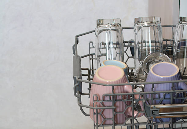 Clean glasses and pastel-colored mugs stand in the open dishwasher after washing, ready for daily use in the kitchen