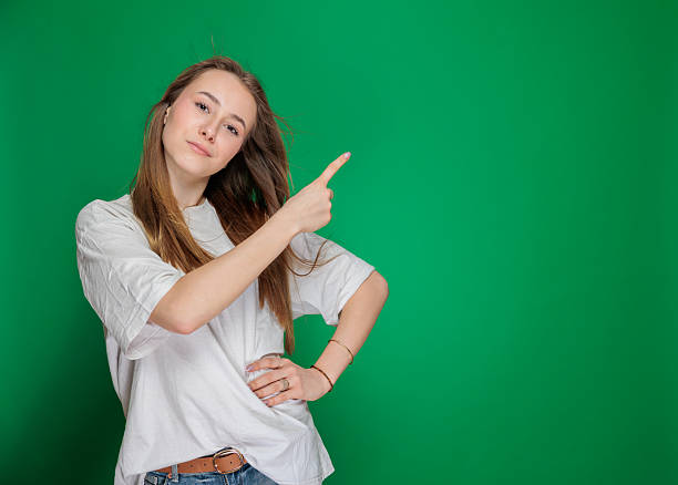 istock Confident Young Woman Pointing to Side on Green Background 2211330150