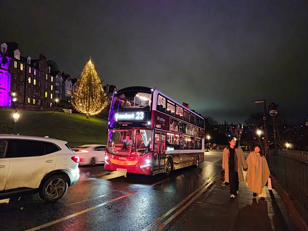 Edinburgh, Scotland, UK - December 14, 2024: Christmas at Edinburgh. A couple walking at The Mound. A double decker bus on the move. Illuminated Christmas Tree, Part of Edinburgh's Christmas