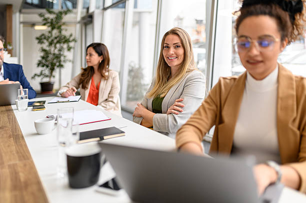 istock Confident female professional with arms crossed smiling at camera while working with coworkers in board room 2211336392