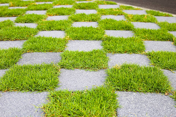 Walkway with a checkerboard pattern, alternating between gray pavement tiles and green grass