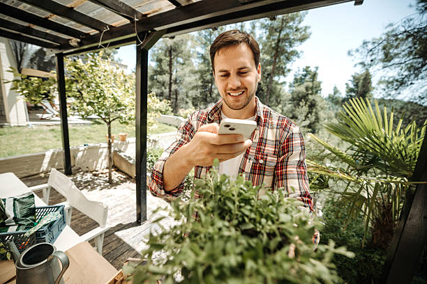 istock Young man photographing potted plants with smartphone in backyard 2211341942