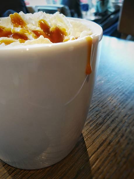 A colour photograph of a mug of coffee with cream and caramel drizzle, and the caramel is dripping down the side of the cup.