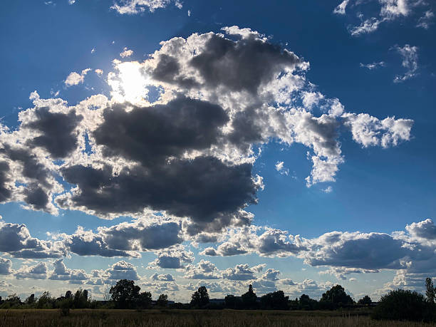 istock Image of a bright day sky with large, fluffy white clouds, one obscuring the sun for an intriguing play of light and shadow Distant landscape of green fields under a blue sky with scattered white cl 2211342761