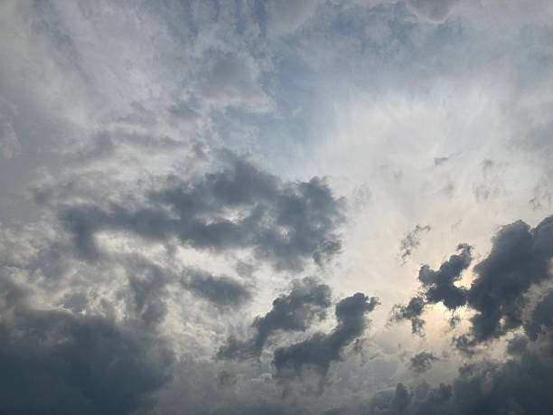 A dramatic sky filled with scattered, fluffy and ominous clouds The silhouette of a celestial body possibly moon is visible through breaks The image captures an angle that emphasizes the grandeur