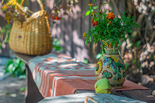 An inviting outdoor setting with rustic elements, a woven table, vase of vibrant flowers, and a large woven basket Background shows a lush garden, ideal for eco-friendly product marketing, outdoor f
