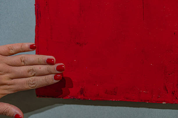 A hand touches a vibrant, abstract red painting against a white backdrop in this image, emphasizing personal interaction with art and artistic expression