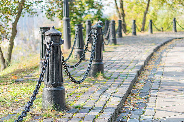 istock A serene, timeless scene showcases an old stone pathway leading through a lush park or garden, surrounded by metal posts and verdant foliage 2211348429
