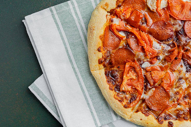 A delicious pepperoni pizza with fresh tomato slices rests on a kitchen towel.