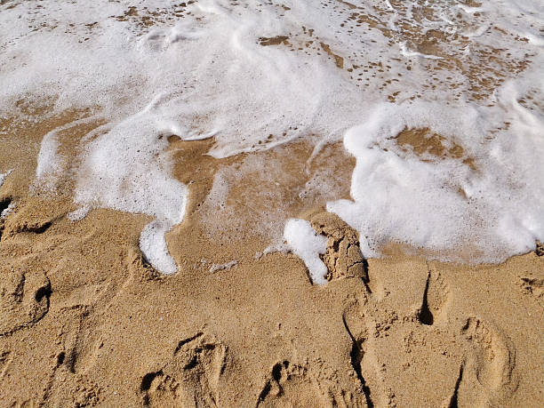 Sandy beach with foamy wave. Evokes peace, travel,  summertime. Ideal for vacation, relaxation, or nature themes. Footprints add a personal touch.