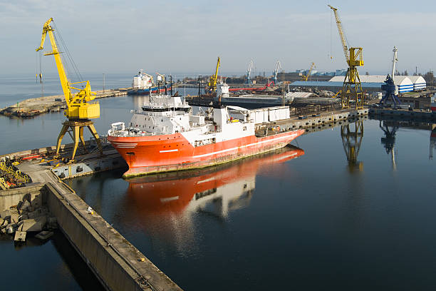 Industrial maritime scene: A large ship undergoing repair or loading at a dock in a busy port with numerous cranes.