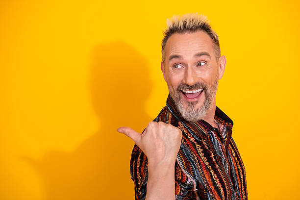 istock Charismatic mature man smiling and pointing over bright yellow background with style 2211387418