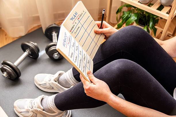 istock Woman sitting on a yoga mat, reviewing her workout plan while preparing for an invigorating fitness session with dumbbells, embodying a commitment to health and wellness 2211387558