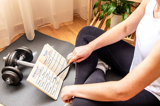 istock Sitting on a yoga mat, a woman points at her workout plan in a notebook, with dumbbells lying nearby, demonstrating her commitment to fitness and a healthy lifestyle 2211387560