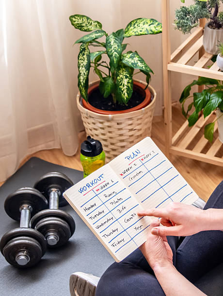 istock Woman sitting on a yoga mat at home, reviewing her workout plan while organizing a weekly fitness routine. Dumbbells and a water bottle rest nearby, enhancing her commitment to a healthy lifestyle 2211387572