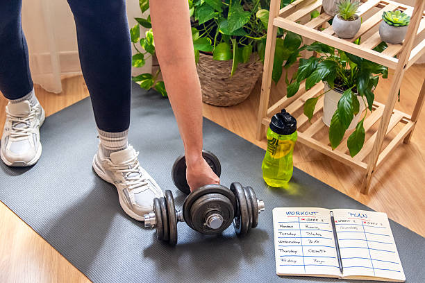 istock Woman picking up dumbbells and preparing to exercise at home, following a structured workout plan, with a refreshing bottle of water and lush houseplants nearby 2211387599