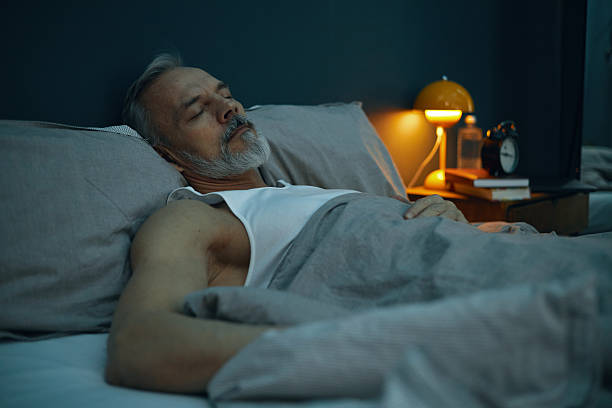 istock Sleeping Elderly Man in Comfortable Bed Next to Lamp 2211389337