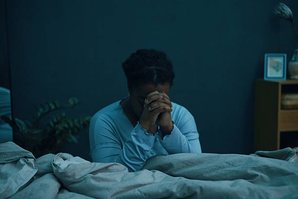 istock Praying Woman Sitting on Bed in Dimly Lit Room 2211389392
