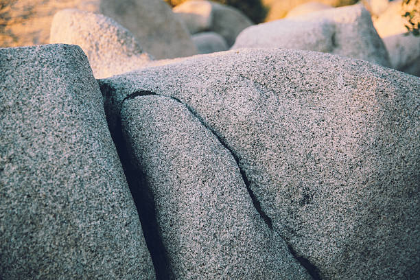 A large rock sits in close focus, split cleanly down the middle as if nature herself made the divide with purpose. Its textured surface catches the soft, golden-blue light, revealing fine cracks and tiny flecks of mineral. The gentle lighting casts a peaceful glow along the broken edge, highlighting both the strength and fragility of the stone. The scene feels still and contemplative, like a quiet pause in time.