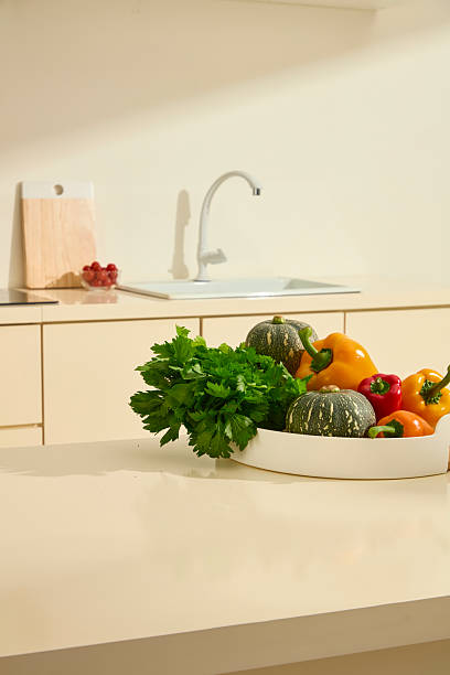 istock Celery, pumpkin, and bell peppers are placed on a tall white round plate on a marble countertop in the kitchen. Behind is a kitchen sink, wooden cutting board and a glass bowl of cherry tomatoes. 2211390416