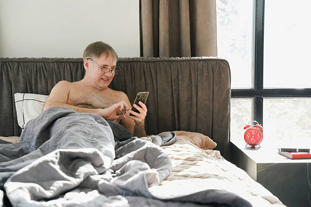 istock Man relaxing in bed using mobile phone while resting comfortably at home. 2211392193