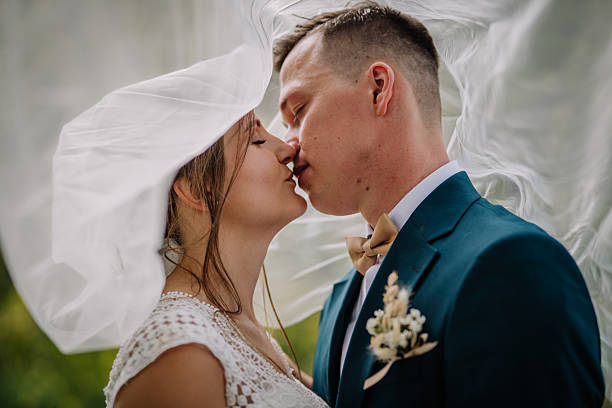 istock Bride and groom share a soft kiss beneath a flowing wedding veil. A romantic and intimate outdoor moment filled with emotion and natural elegance. 2211395122