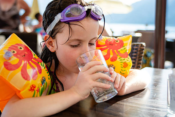 Cute little girl whit swimming goggles drinking sparkling water on a restaurant terrace near the sea