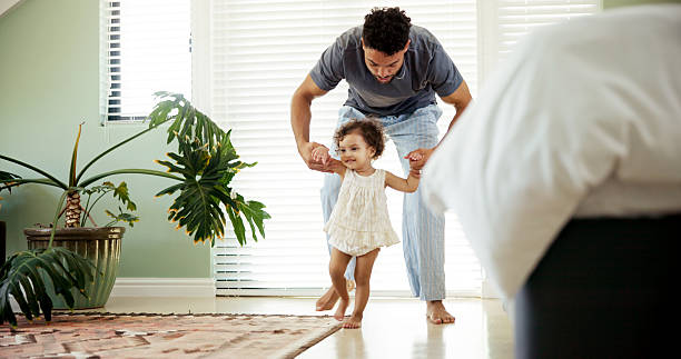 istock Dad, toddler or learning to walk in home with holding hands, first steps or helping with balance. Happy family, child or man with teaching coordination in bedroom with mobility support or development 2211398462