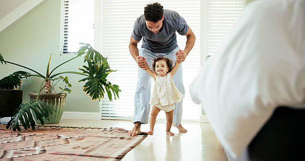 istock Father, child and learning to walk in home with holding hands, first steps and support with mobility. Happy family, toddler and man with teaching balance in bedroom for practice or growth development 2211398471