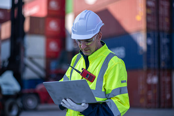 istock Dock worker or engineer overseeing operations logistics and shipping yard managing inventory, shipping schedules, or container tracking technology, and safety in the shipping industry, depicting a professional in action at a container yard. 2211399971