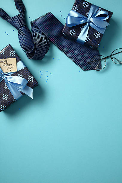 istock Father's Day flat lay concept with gift boxes, necktie, eyeglasses, and confetti on a blue background. Top view with copy space for holiday greetings 2211400013