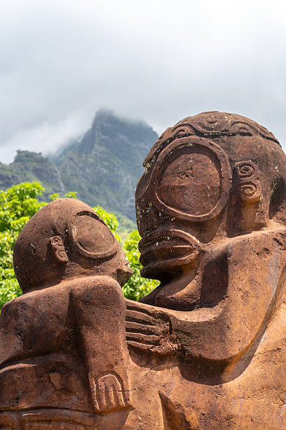 A majestic tiki statue stands before Mount Temetiu on Hiva Oa, French Polynesia. This stone carving represents the rich cultural heritage of the Marquesas Islands, blending history and nature