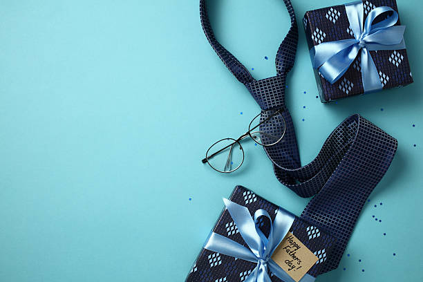 istock Stylish Father's Day concept: flat lay with blue tie, eyeglasses, and two gift boxes on blue background. Top view, copy space. 2211400594