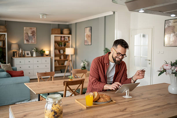 istock Smiling man making online payment while having breakfast in modern apartment 2211402560
