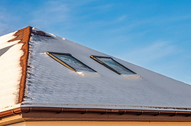 A rooftop covered with a thick blanket of snow, two skylights peering through the crisp, blue sky above.