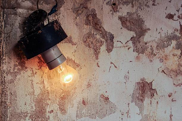 A vintage lightbulb illuminates a distressed wall, creating a contrast between light and texture in this evocative image.