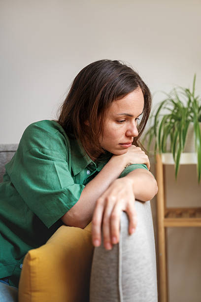 istock Sad and tired woman sitting on sofa at home looking down 2211406967