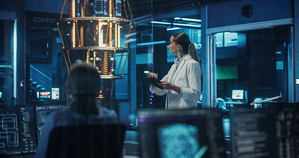 istock Beautiful Female Computer Scientist in a Lab Coat Walking Up to a Quantum Computer in a Futuristic Laboratory. Young Caucasian Researcher Analyzing Complex Computing Data on a Tablet 2211413497
