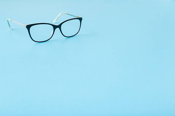 istock Eyeglasses with dark black plastic frame on light blue table background. Pastel color. Closeup. Empty place for text. Front view. 2211418040